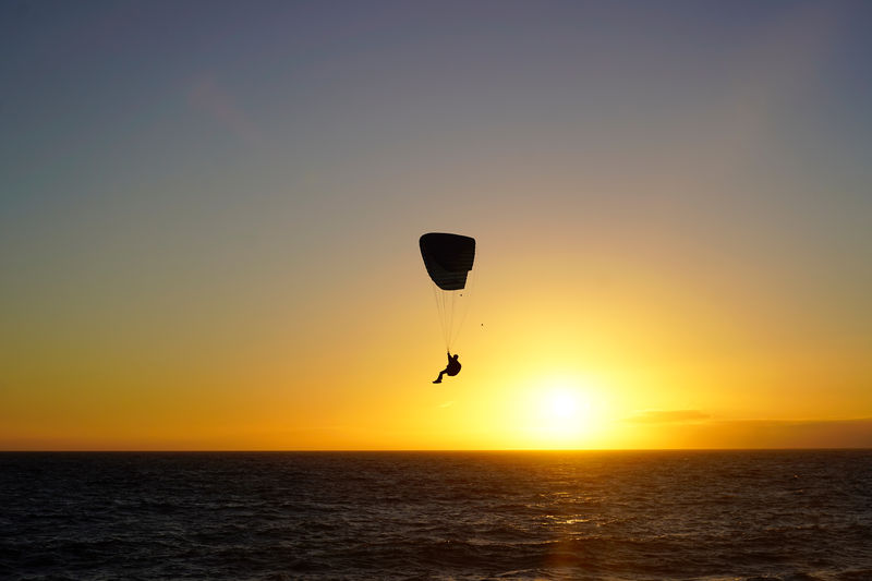 Silhouette of a person paragliding during sunset, over the beach