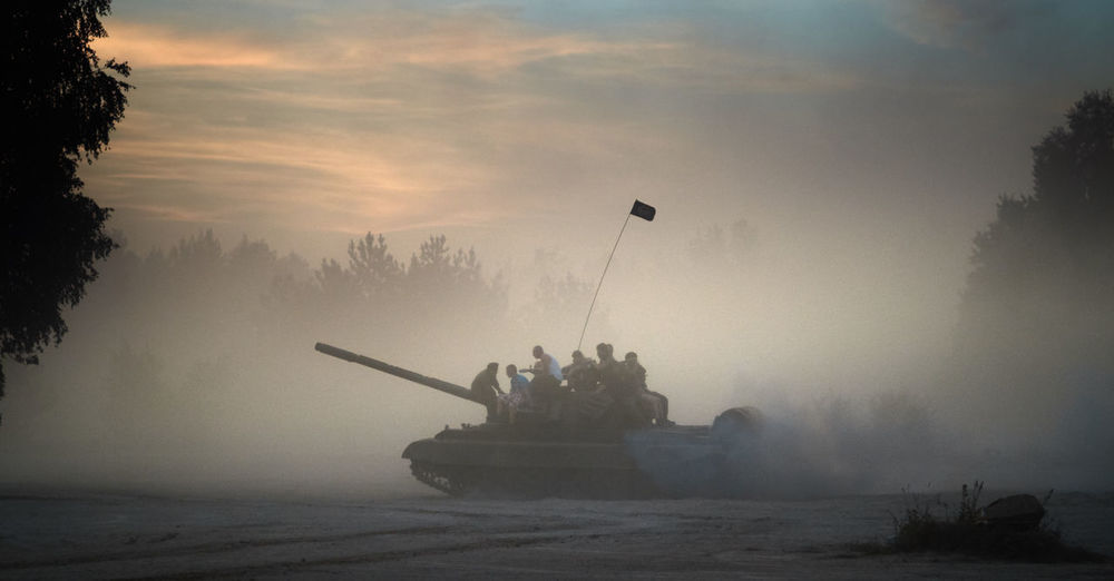 People sitting on military tank in foggy weather against sky at borne sulinowo