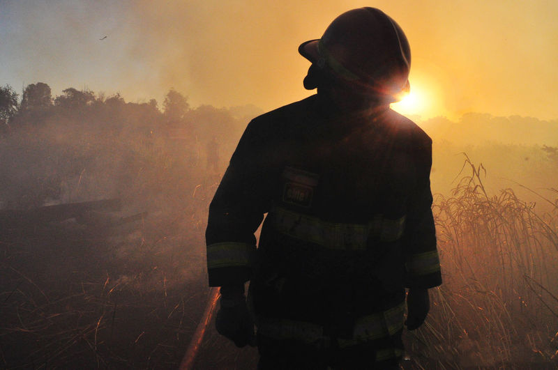 Firefighter walking on field against sky during sunset