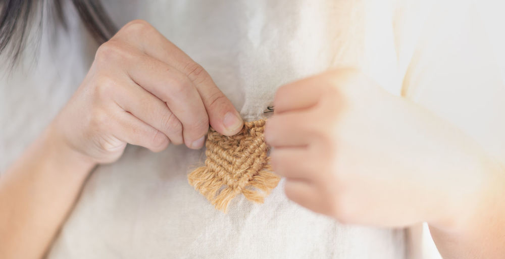 Female hand sticking the hand-made brown macramé brooch on the cotton shirt. 