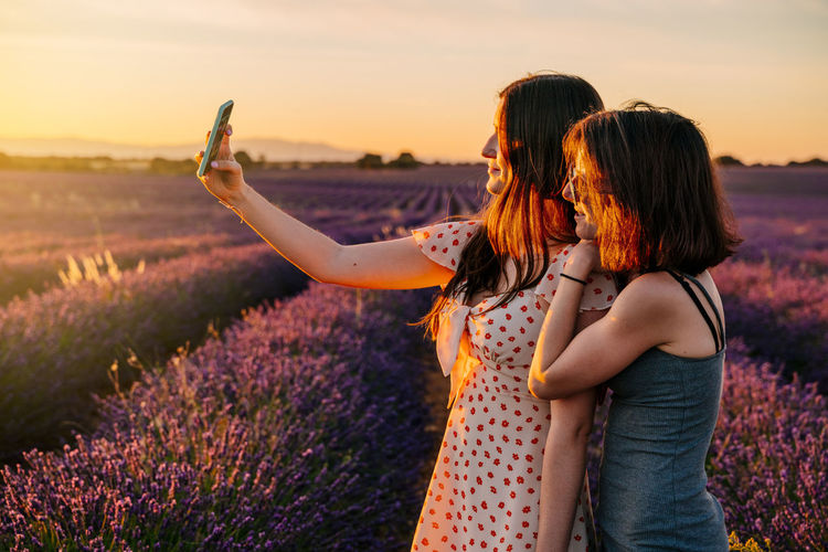 Women taking selfie while standing on field against sky during sunset