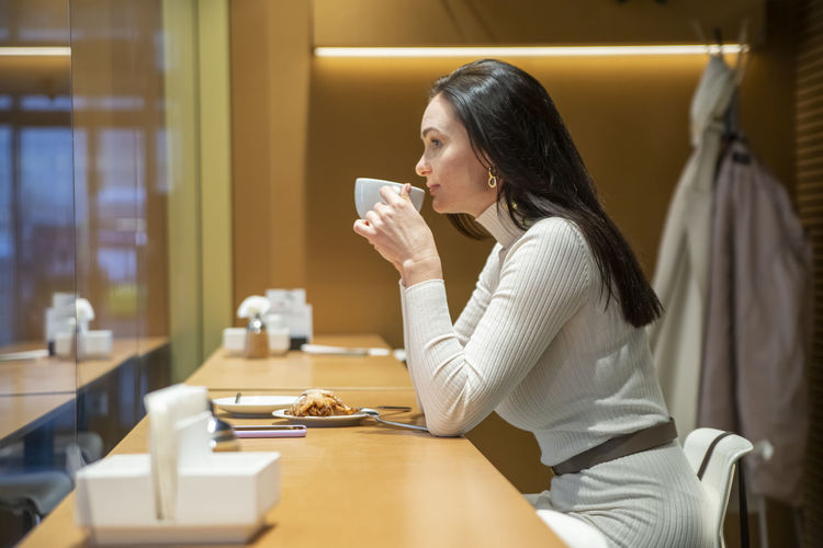 Young woman drinking coffee while sitting on table
