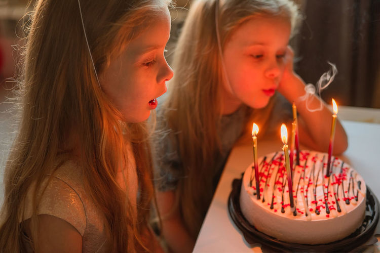 Little twin girls, children blow out candles cake birthday party at home. holiday during quarantine