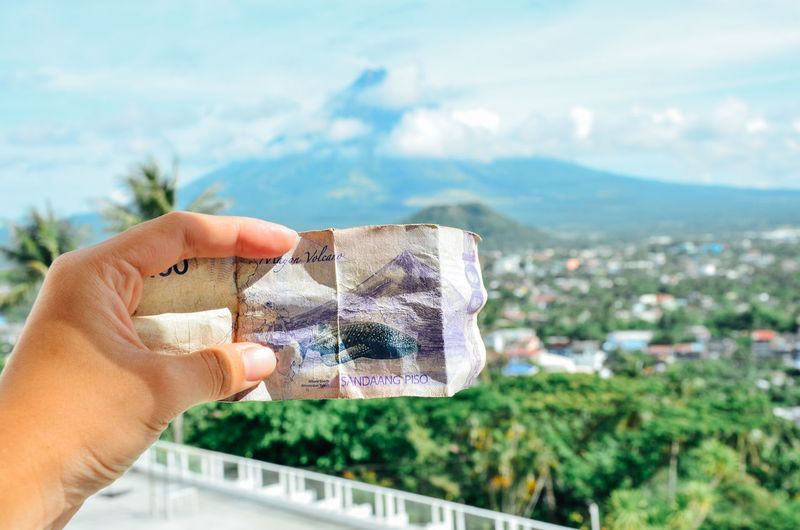 Cropped hand holding paper currency against mountain