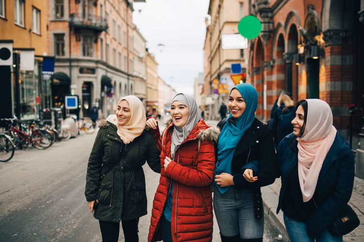 Happy multi-ethnic muslim female friends standing on street in city