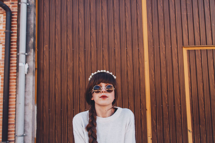 Portrait of woman wearing sunglasses while standing against wall