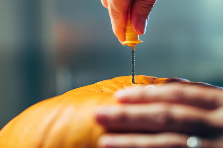Cropped hand of person drilling in pumpkin