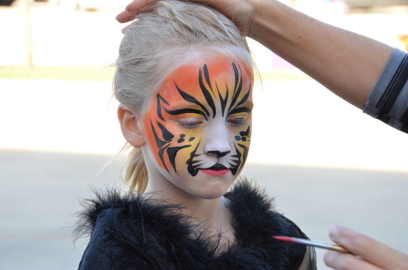 Artist applying tiger paint on girl during halloween