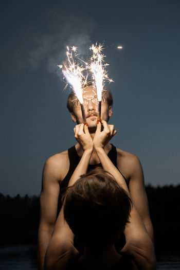 Midsection of woman holding sparkler against sky