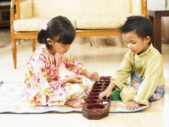 Siblings playing while sitting on floor at home
