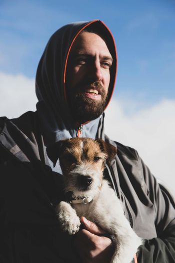 Man in hood carrying dog against sky
