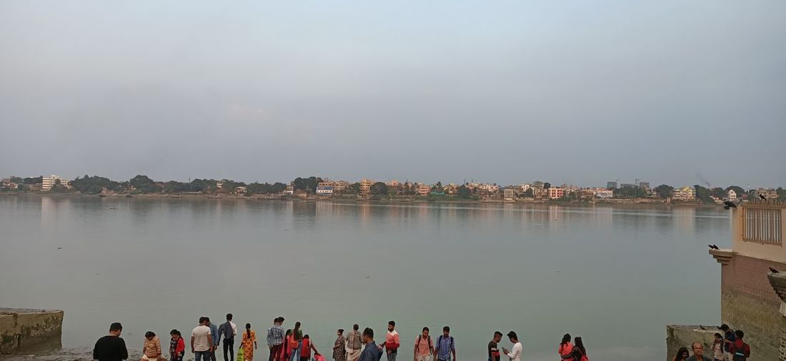 People by lake against sky