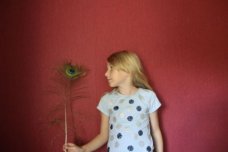 Girl holding peacock feather against wall