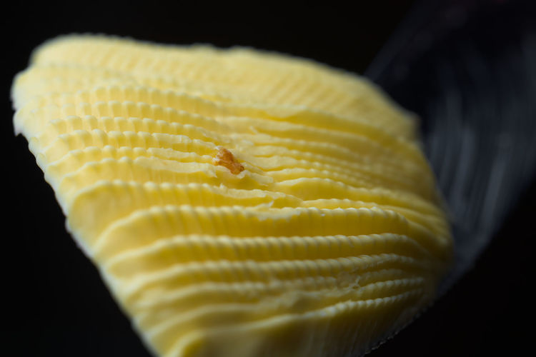 Serrated knife holds a fan shaped curl of rippled yellow margarine. isolated on black background