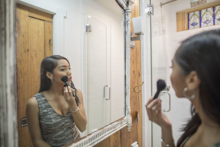 Young woman applying makeup in her bathroom mirror