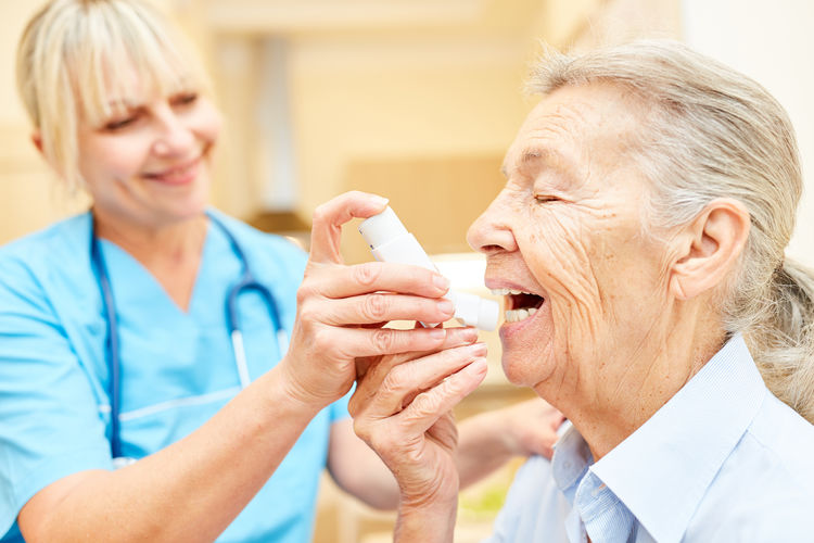 Smiling nurse assisting senior patient using inhaler