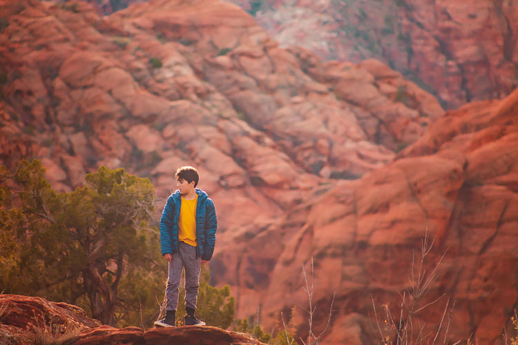 Boy hiking on trail by the red sandstone cliffs and mountains in utah
