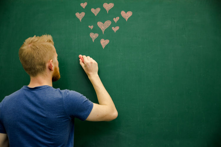 Rear view of young man with eraser by heart shape drawing on blackboard