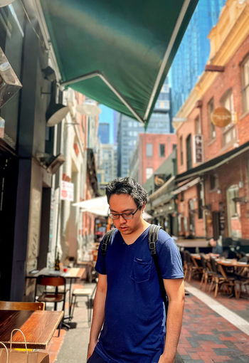 Portrait of young asian man standing against buildings in laneway in the city.