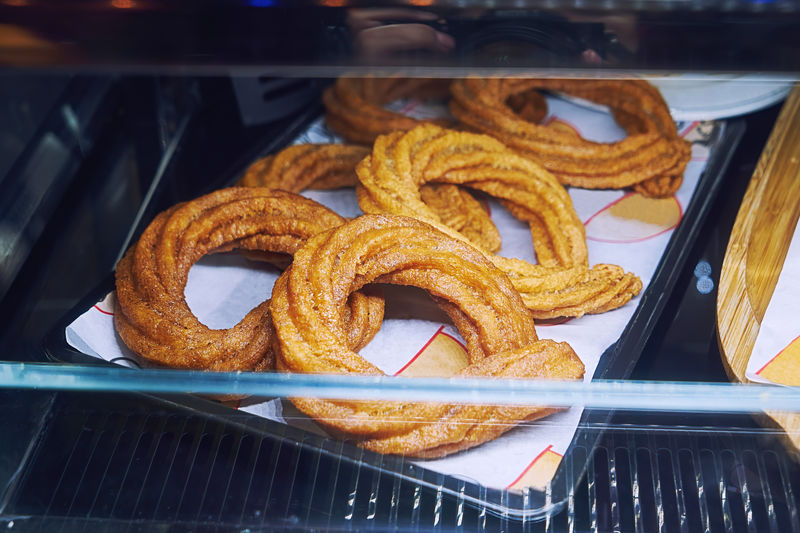 Sweet baked churros pretzel with cinnamon and caramel on counter in street cafe, closeup