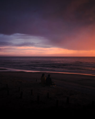 Blue hour scene with dramatic sky and couple sitting enjoying the beach