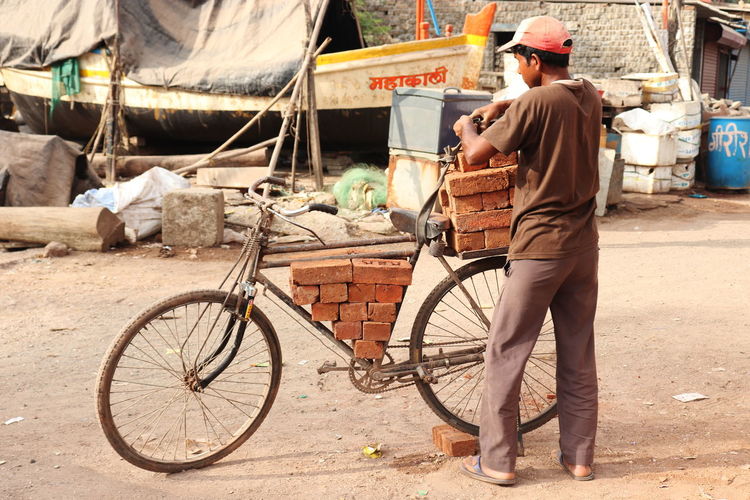 Rear view of a young man arranging bricks in an innovative manner on a bicycle for transporting