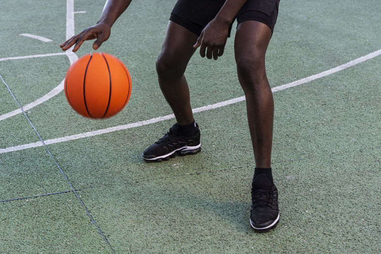 Cropped unrecognizable african american male playing basketball on modern sports ground during training