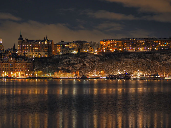 Illuminated buildings by river against sky at night