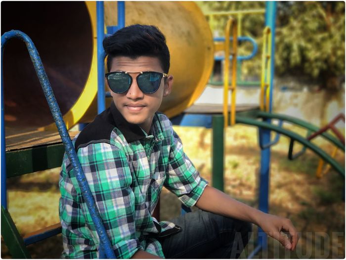 Portrait of young man wearing sunglasses while sitting on outdoor play equipment