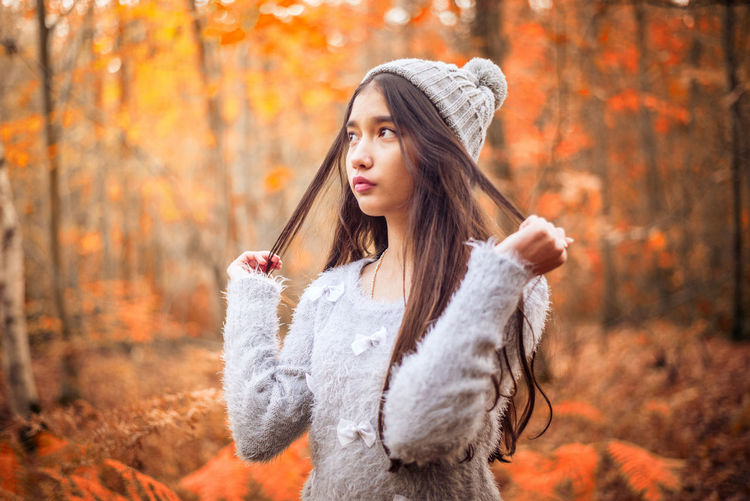 Teenage girl looking away while standing in forest during autumn