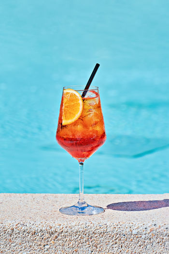 Wine glass of cold cocktail aperol spritz against turquoise water of poolside