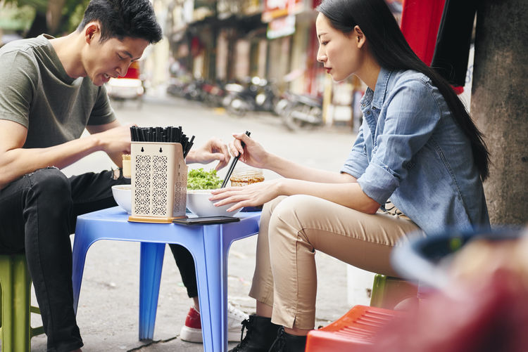 Young couple eating food while sitting outdoors