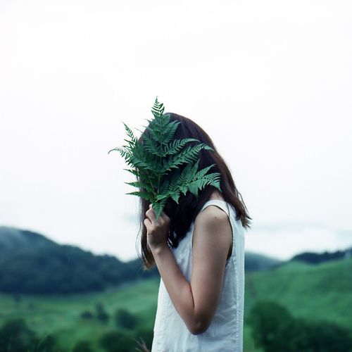 Side view of young woman covering face with leaves