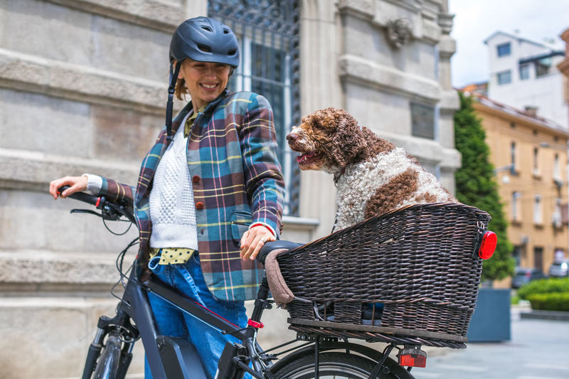 Young woman pushing her electric bicycle with the dog in the basket
