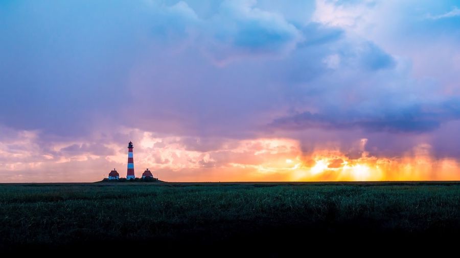 Lighthouse on field against sky during sunset