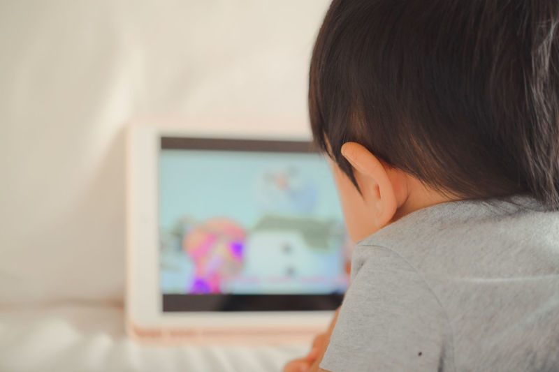 Rear view of boy using mobile phone at home