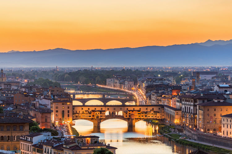High angle view of ponte vecchio over river amidst buildings against sky during sunrise