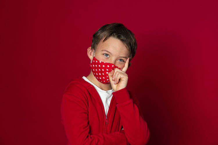 Cute boy wearing mask against red background