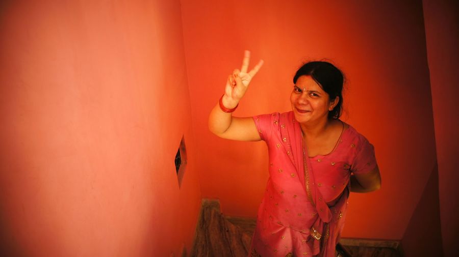 High angle portrait of smiling woman gesturing peace sign at home