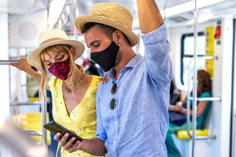 Smiling couple wearing mask using smart phone standing in bus