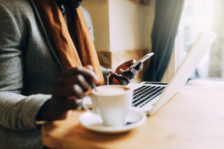 Midsection of man using mobile phone while having coffee in cafe