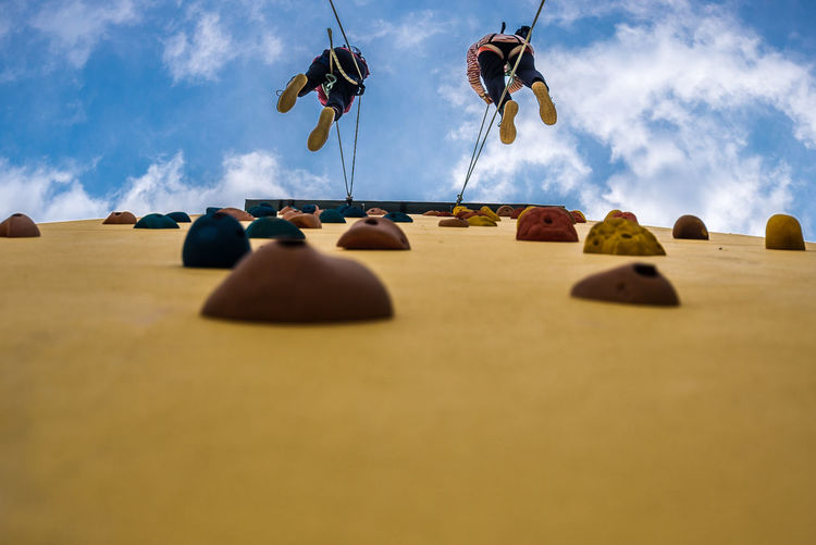 Low angle view of people climbing on wall against sky