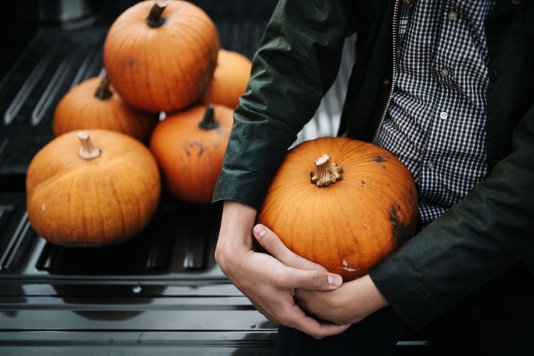 Midsection of man holding pumpkin while sitting outdoors