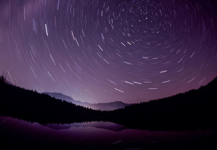 Scenic view of silhouette mountains against sky at night with star trails 