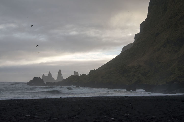 Rocks on beach against cloudy sky