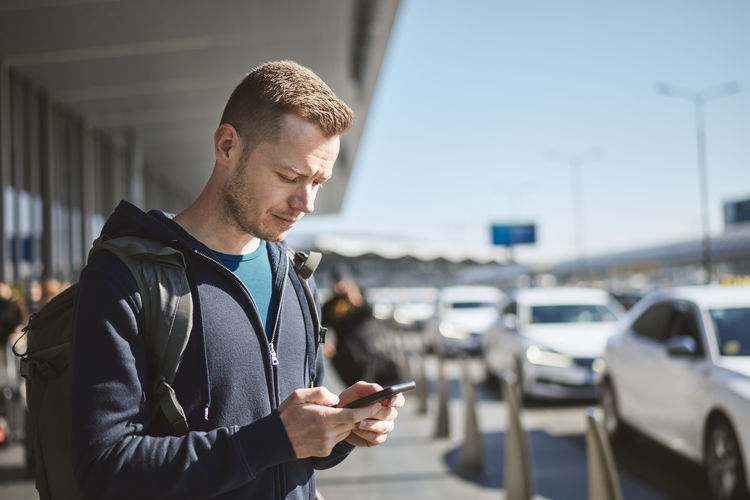 Man holding smartphone and using mobile app against a row of taxi cars. 
