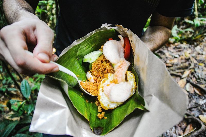 Close-up of man holding nasi goreng or indonesian fried rice while trekking the jungle
