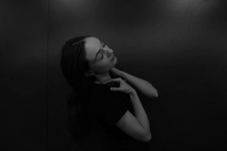Portrait of woman looking away while standing against black background