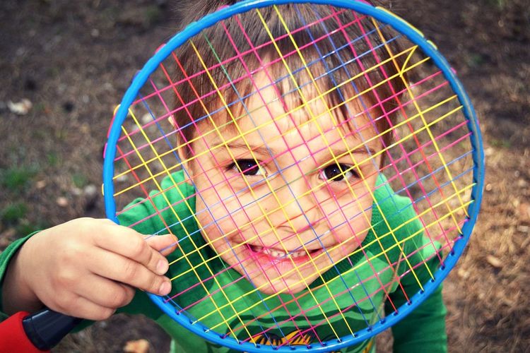 Portrait of happy boy looking through badminton racket