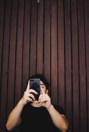 Young man using mobile phone while standing by wall